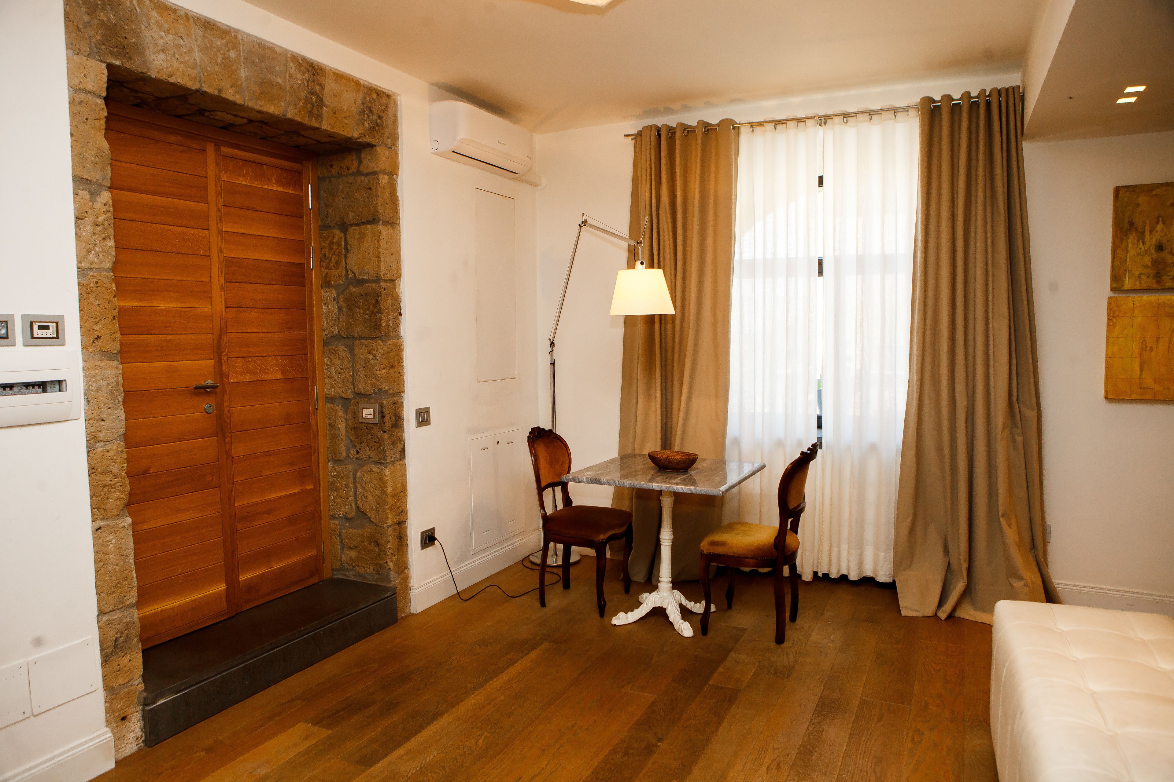 Une pièce avec une porte en bois, une table à manger avec des chaises, une lampe et un lit.