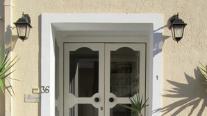 Une porte double blanche avec des panneaux de verre, un petit porche avec des marches et deux lanternes fixées au mur.
