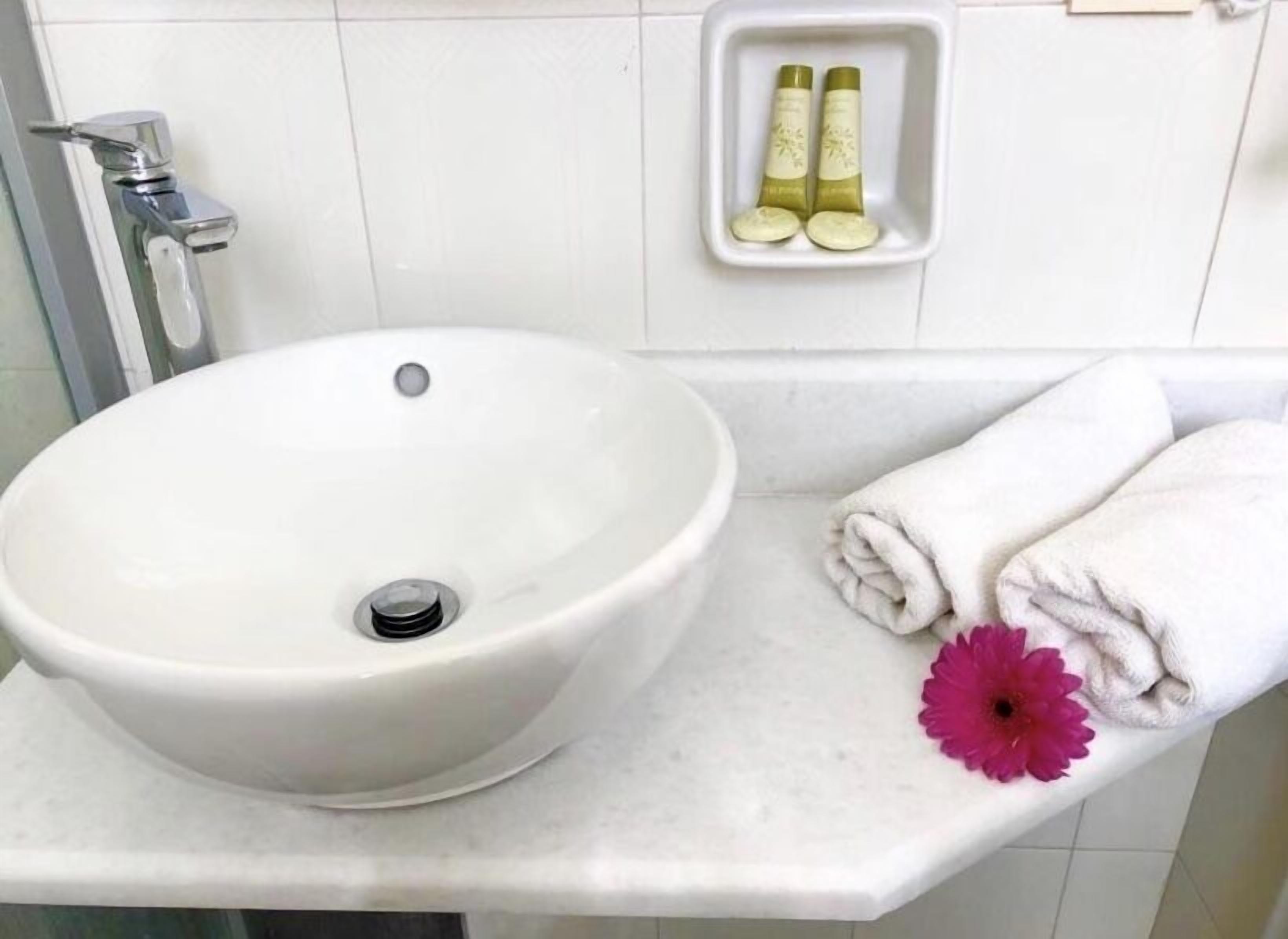A bathroom with a white sink, a towel rack with folded towels, and a small shelf with two bottles.
