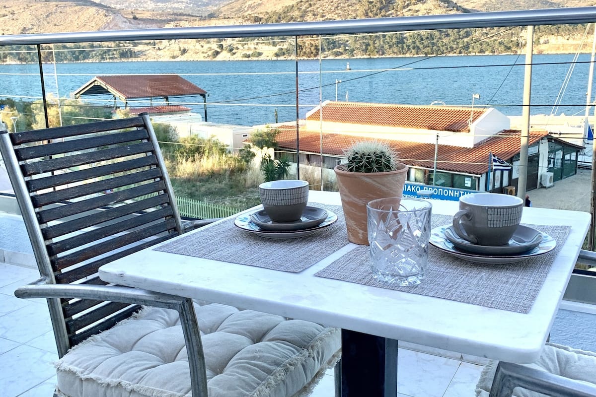 Um terraço com mesa e cadeiras, com vista para um corpo de água e montanhas.
