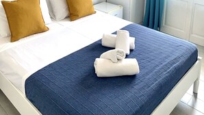 Une chambre d’hôtel avec un lit, un tableau représentant un paysage côtier, une armoire et une fenêtre avec des rideaux.