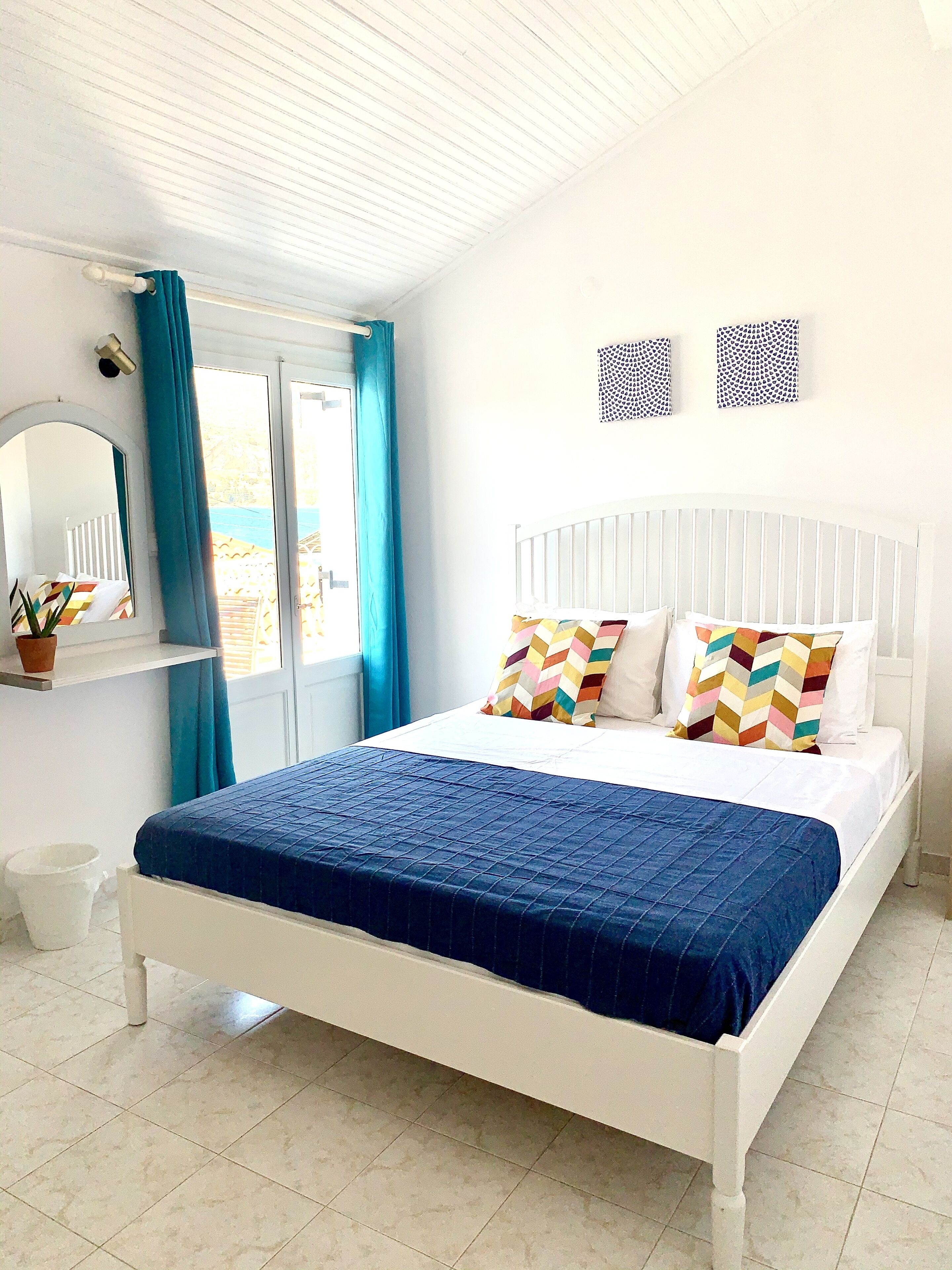 Un dormitorio con una cama blanca, una colcha azul y dos almohadas estampadas.