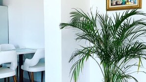 Une pièce avec une table et des chaises blanches, une plante en pot et un tableau encadré accroché au mur.