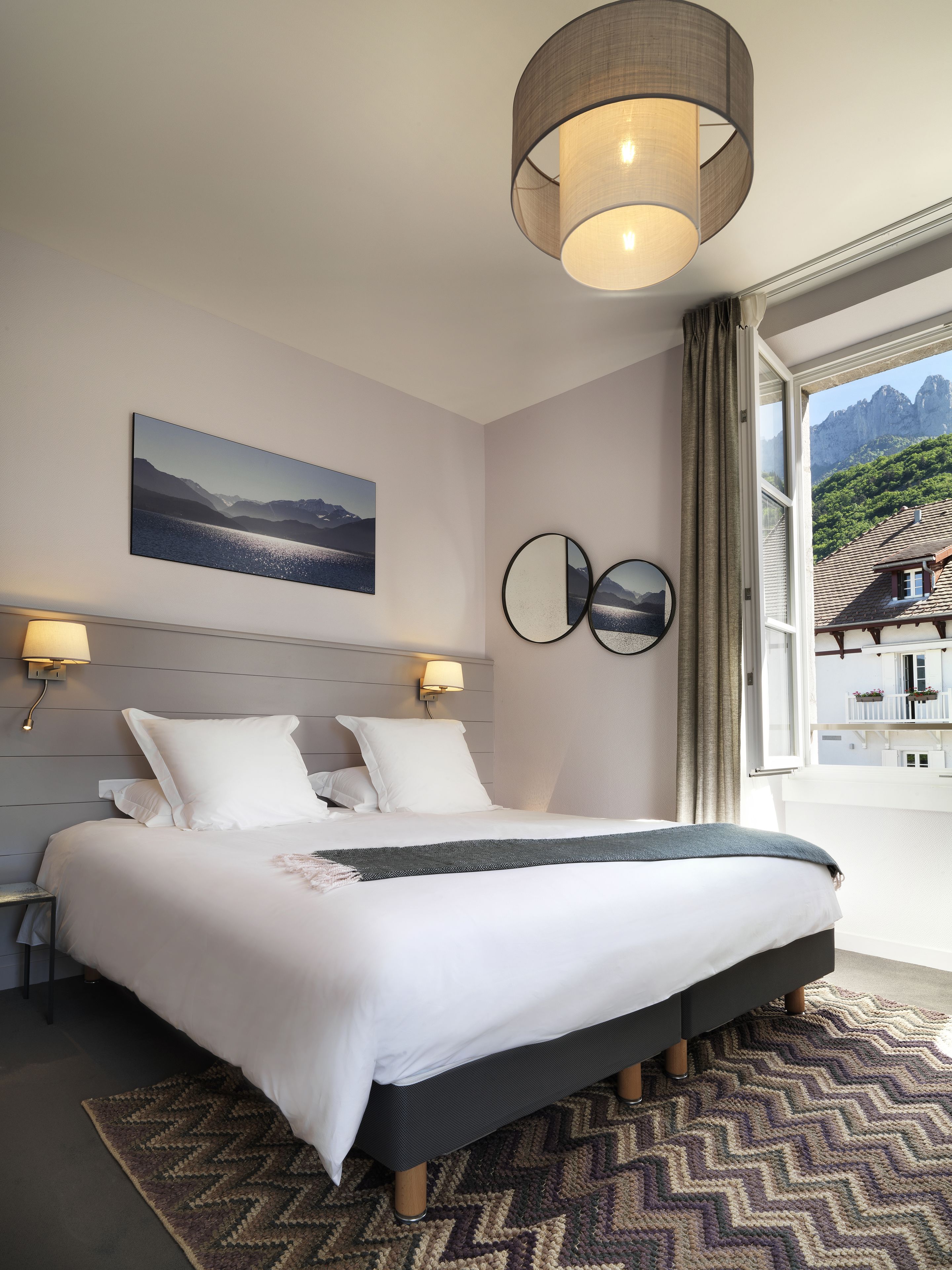 Une chambre à coucher moderne avec un grand lit, une vue sur les montagnes par la fenêtre et un tableau accroché au mur.