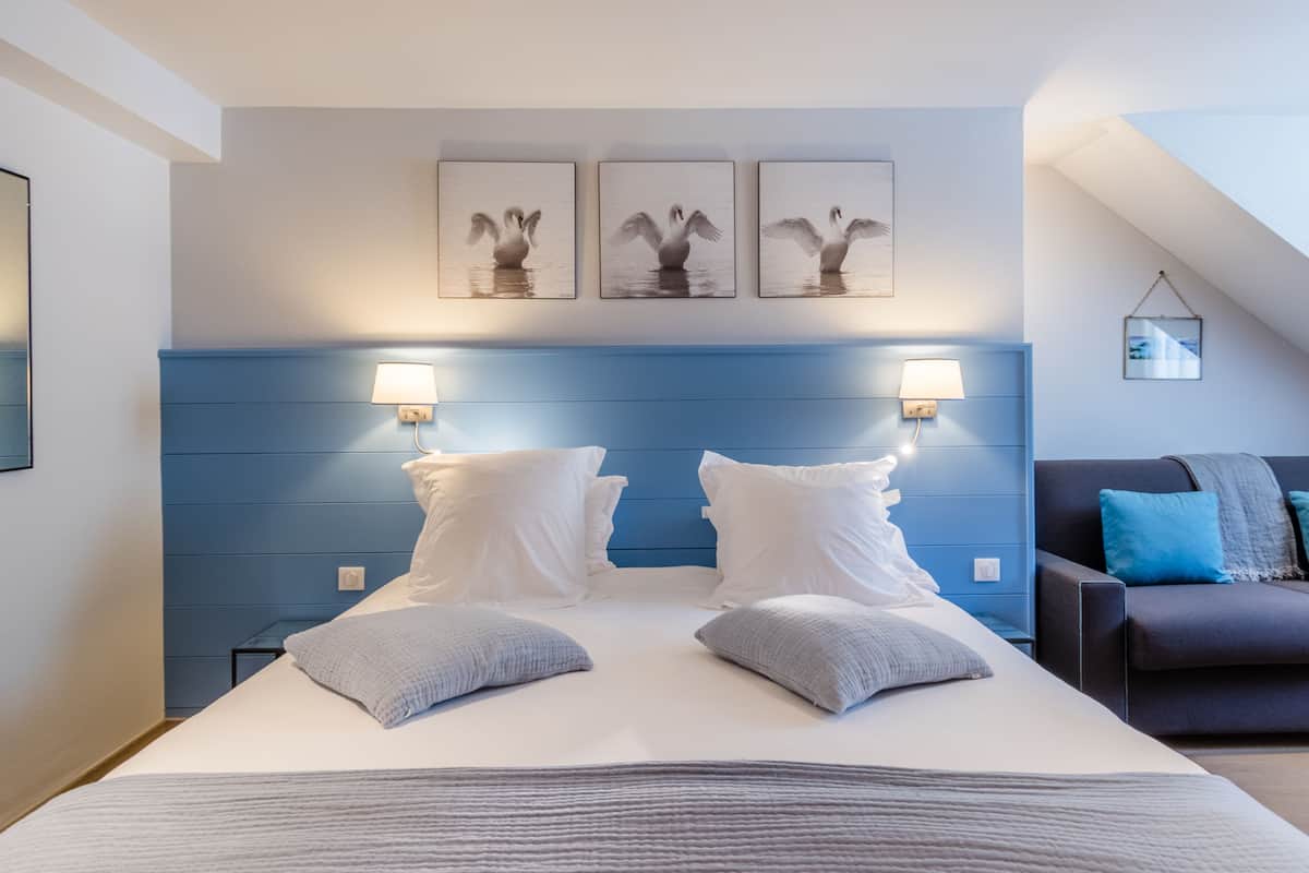 Une chambre d’hôtel moderne avec un grand lit, deux lampes de chevet et une tête de lit bleue.