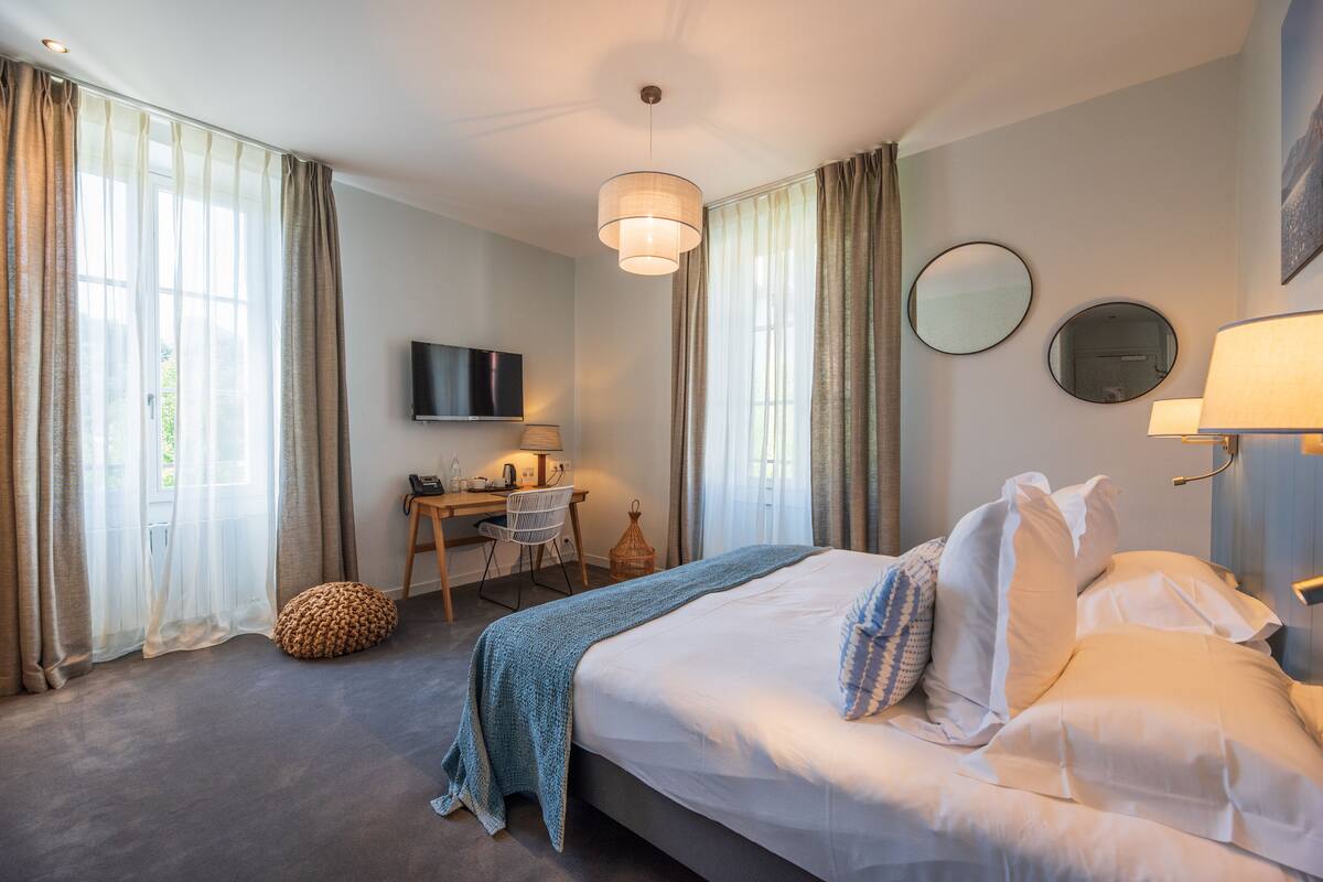 Une chambre d’hôtel avec un grand lit, un bureau avec une chaise, une télévision et une fenêtre avec des rideaux.