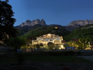 A large, multi-story building with a prominent balcony, surrounded by lush greenery and mountains in the background. - Hotel Beau Site (Talloires-Montmin)