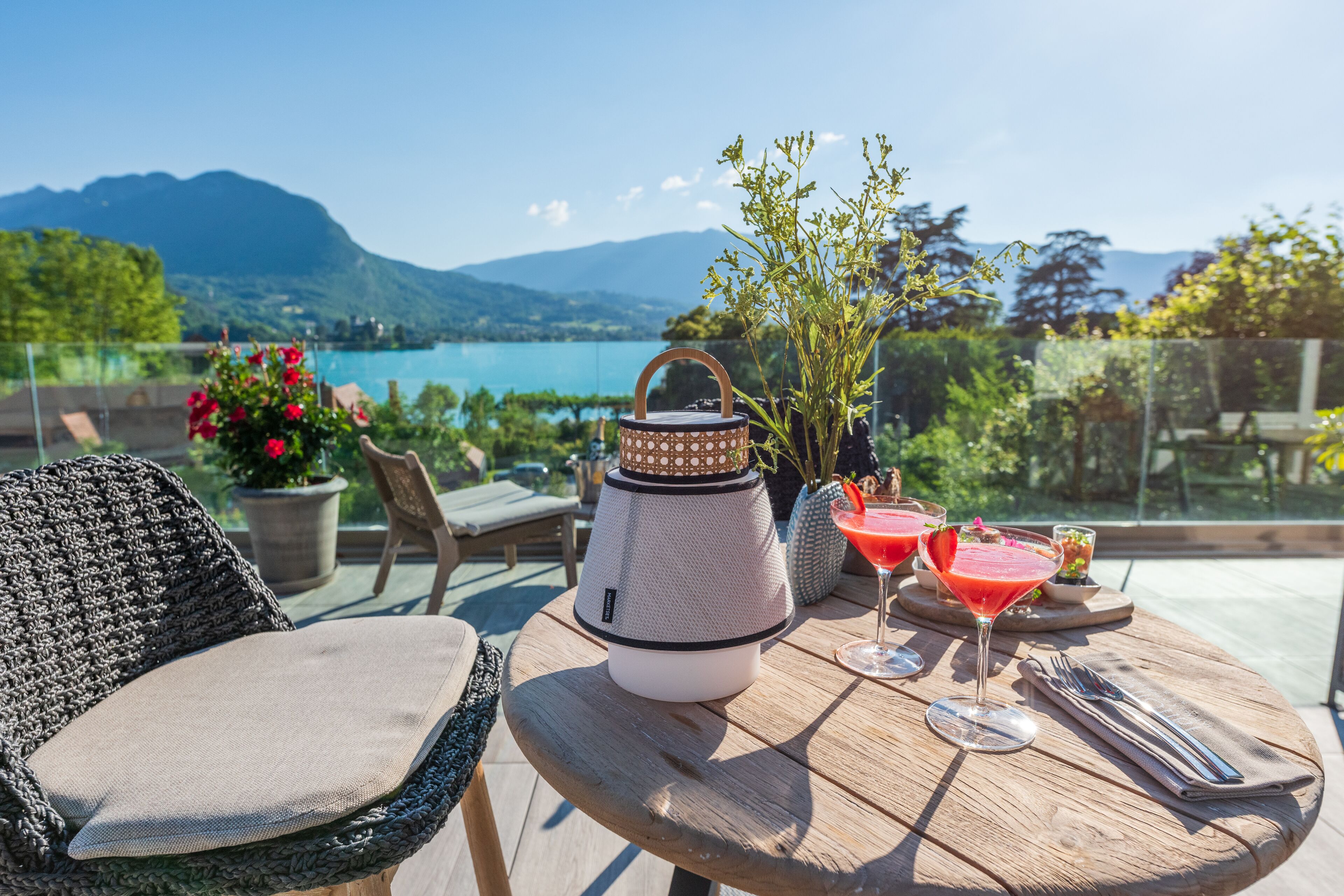 A table with a teapot, drinks, and a view of mountains and water.