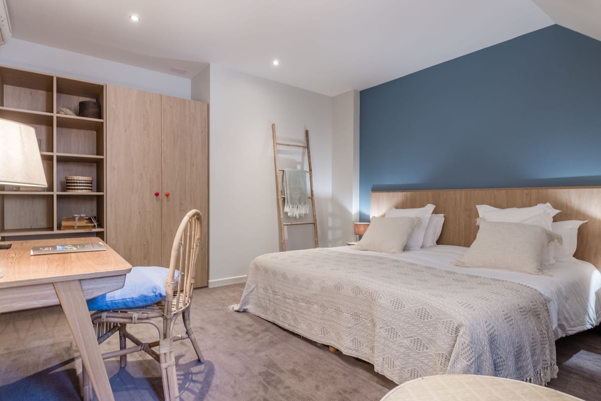 Une chambre avec un bureau en bois, une chaise, un lit avec une literie blanche et un mur d’accent bleu.