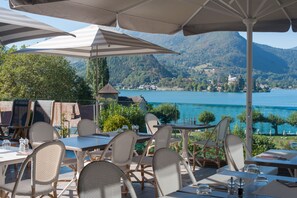 An outdoor dining area with tables and chairs, overlooking a lake and mountains. - Hotel Beau Site (Talloires-Montmin)