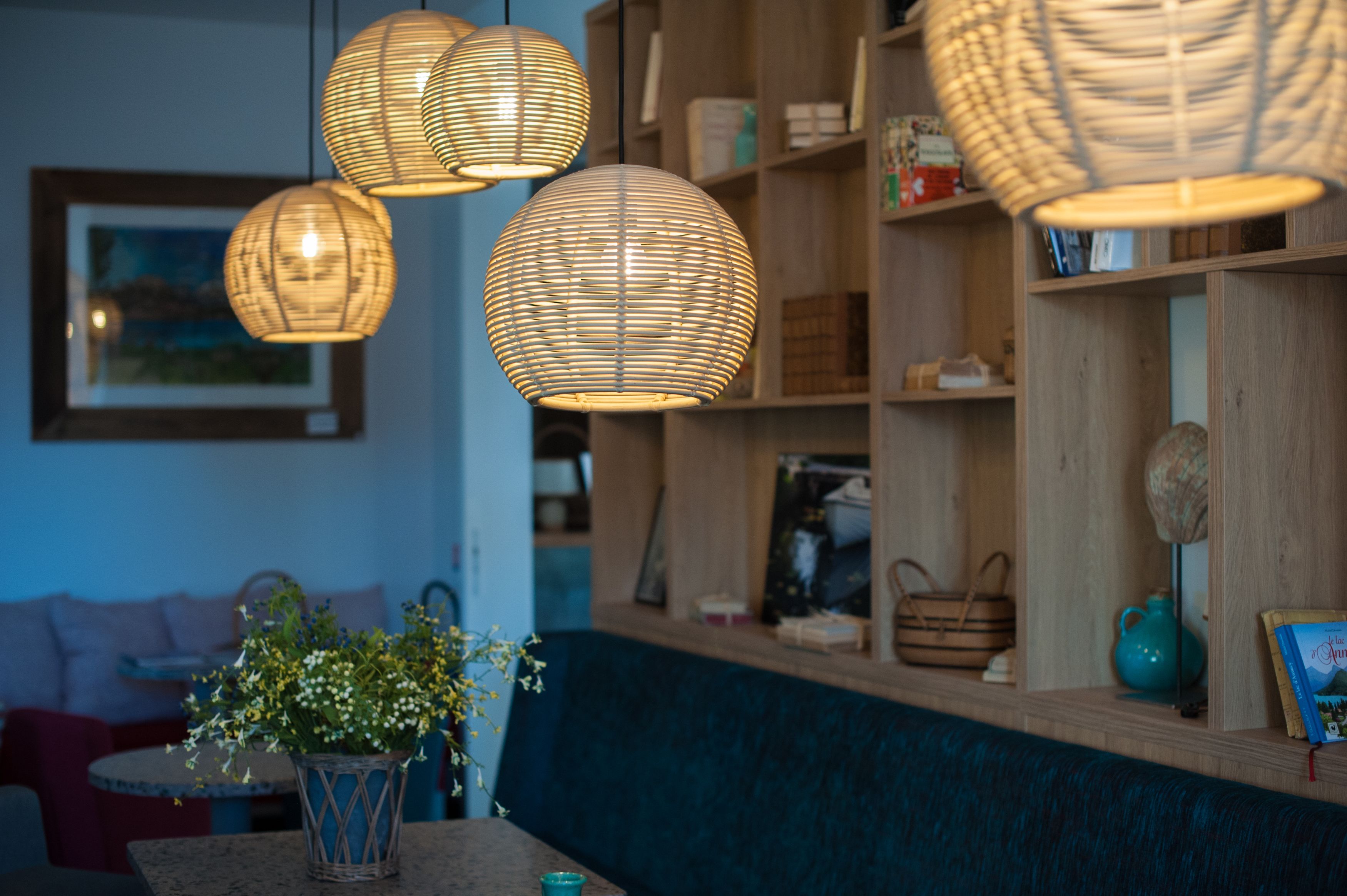 Un interior acogedor con lámparas colgantes de mimbre, una estantería de madera y un banco tapizado en azul.