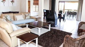 A living room with a sofa, coffee table, and a fireplace. There is a dining area with chairs and a table. - The Old Hatchery (Drakensberg Gardens)