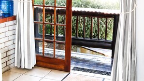 A room with a sliding glass door leading to an outdoor area with a wooden deck and a metal railing. - The Old Hatchery (Drakensberg Gardens)