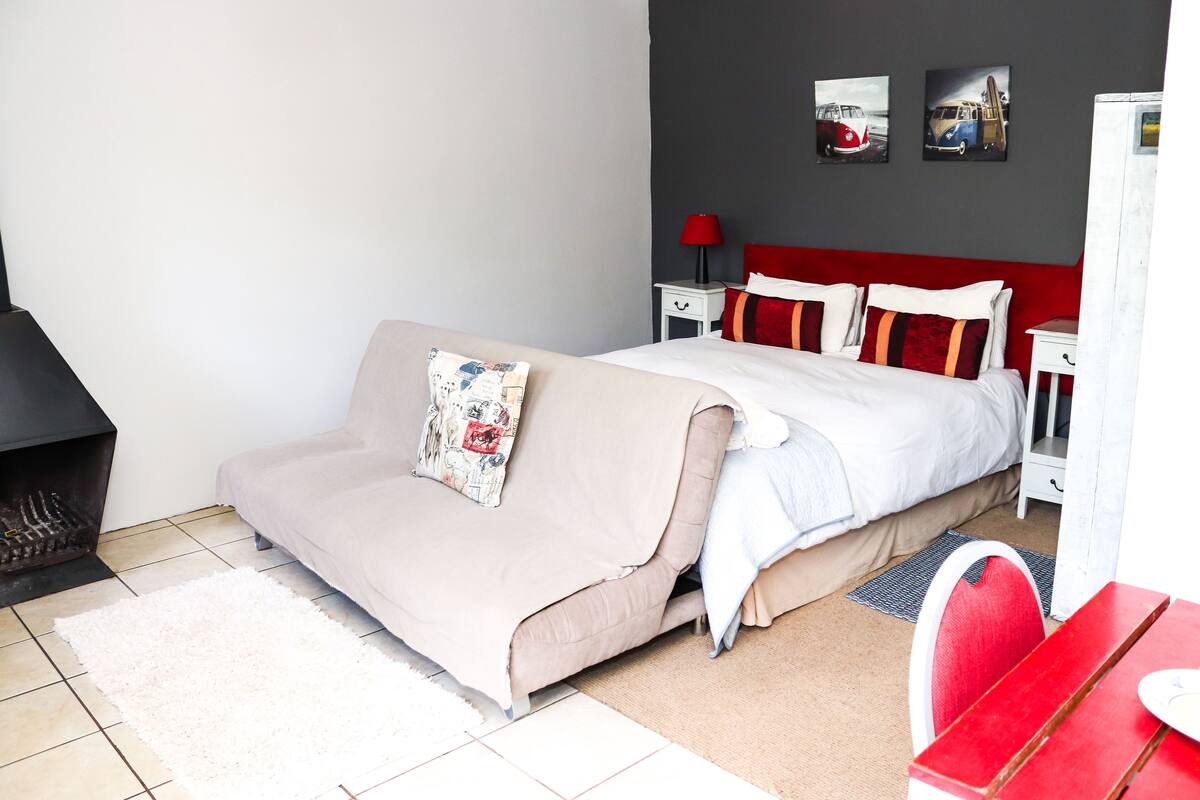 A bedroom with a bed, a sofa, a red table, and a white wardrobe.