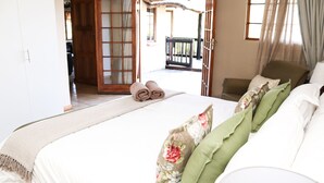 A hotel room with a bed, a chair, and a view of the outside. - The Old Hatchery (Drakensberg Gardens)