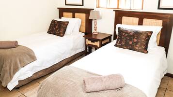 A hotel room with two beds, each with a pillow and a blanket. There is a nightstand with a lamp between the beds.