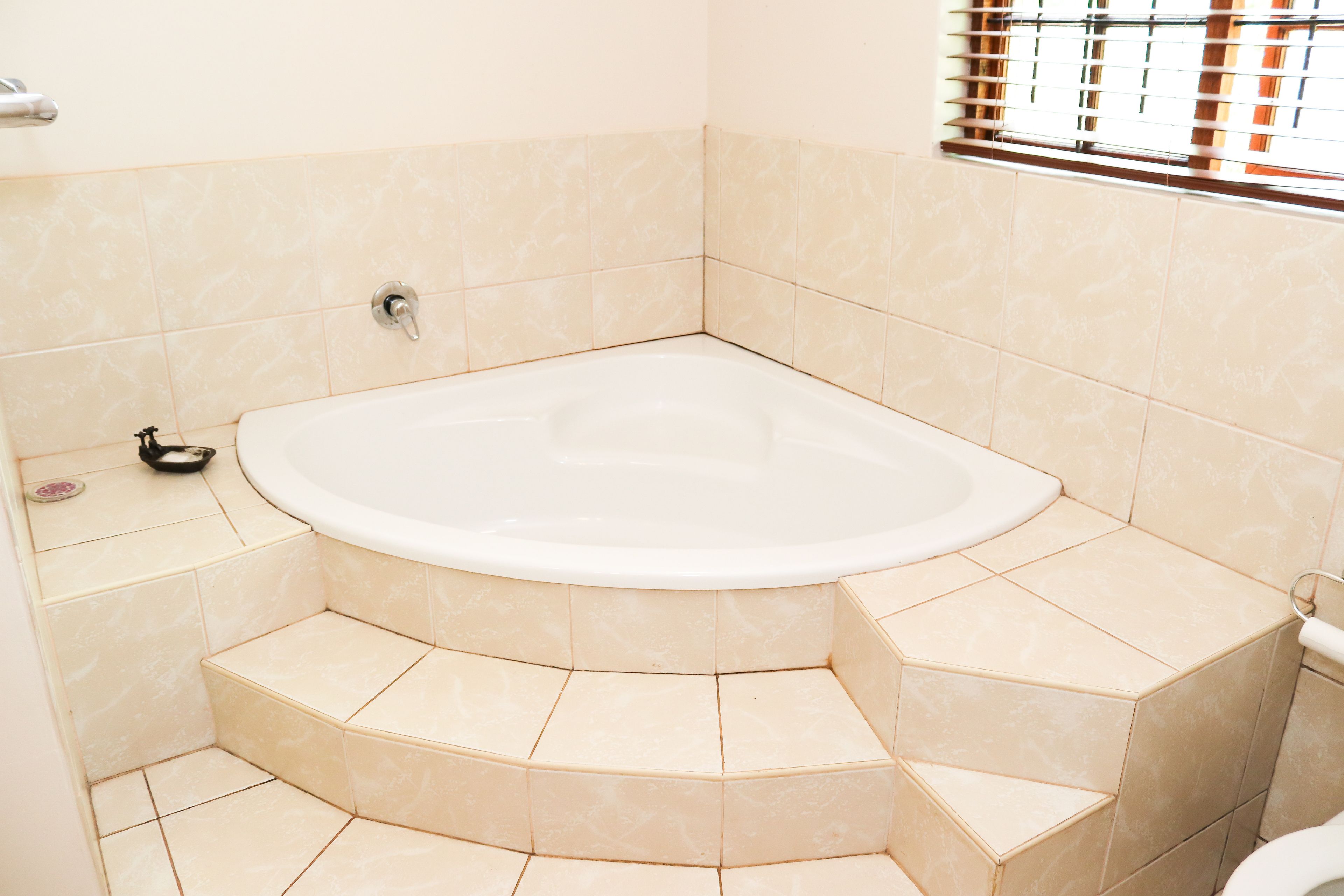 A modern bathroom with a freestanding bathtub, tiled walls, and a window with blinds.