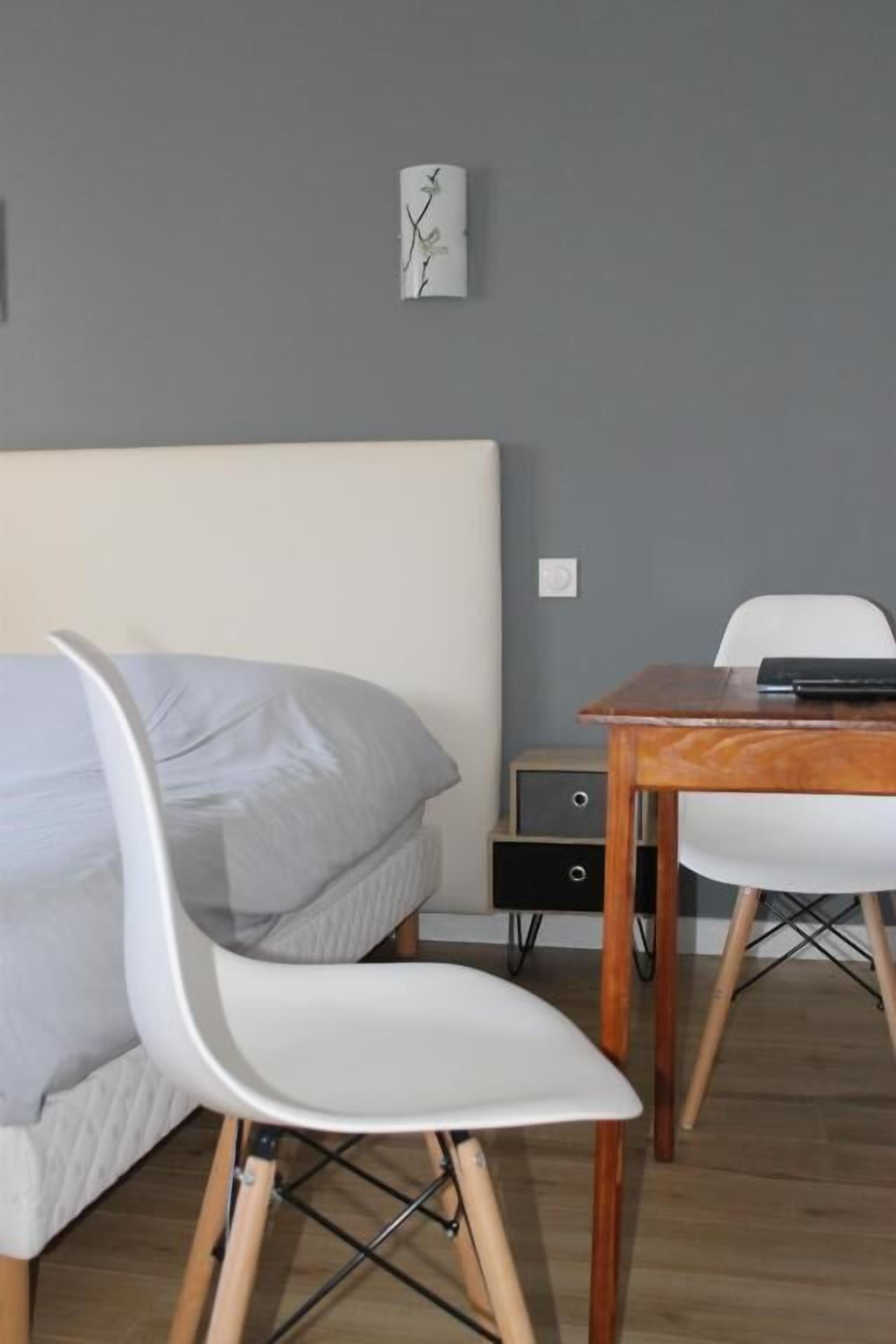 Un dormitorio moderno con una cama, una silla blanca, una mesa de madera y un escritorio pequeño.