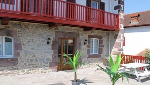 A stone building with a red balcony, a door, and two potted plants. - Auberge Etchoinia (Lasse)