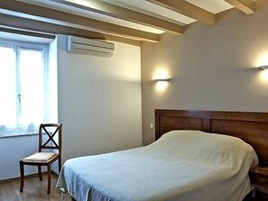 A bedroom with a bed, a chair, a window, and an air conditioning unit. - Auberge Etchoinia (Lasse)