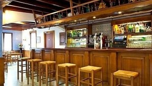 A bar area with wooden stools, a counter with various bottles, and a ceiling with exposed beams. - Auberge Etchoinia (Lasse)