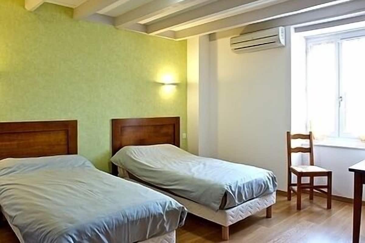 A room with two single beds, a wooden chair, a small table, and a window with natural light.