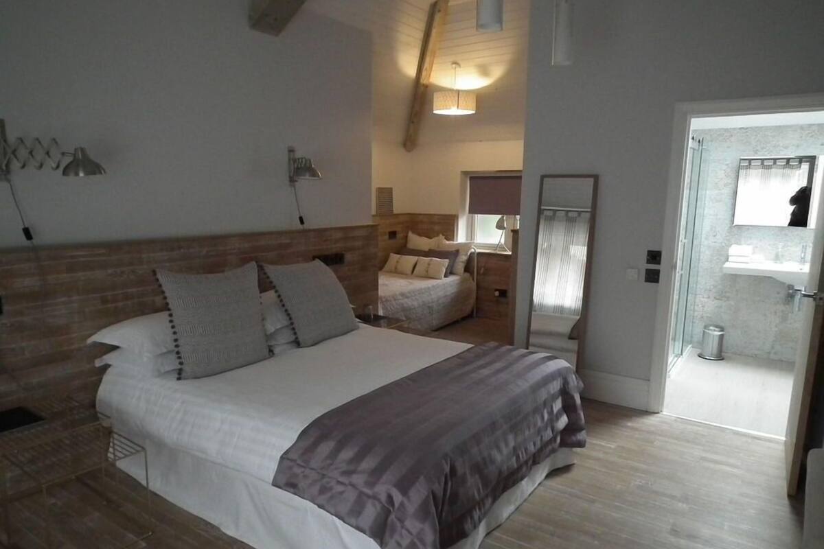 A bedroom with a large bed, a bedside table, a mirror, and a bathroom visible through an open door.