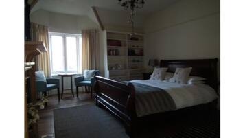 A bedroom with a large bed, a desk, and a chair. There is a bookshelf and a chandelier.