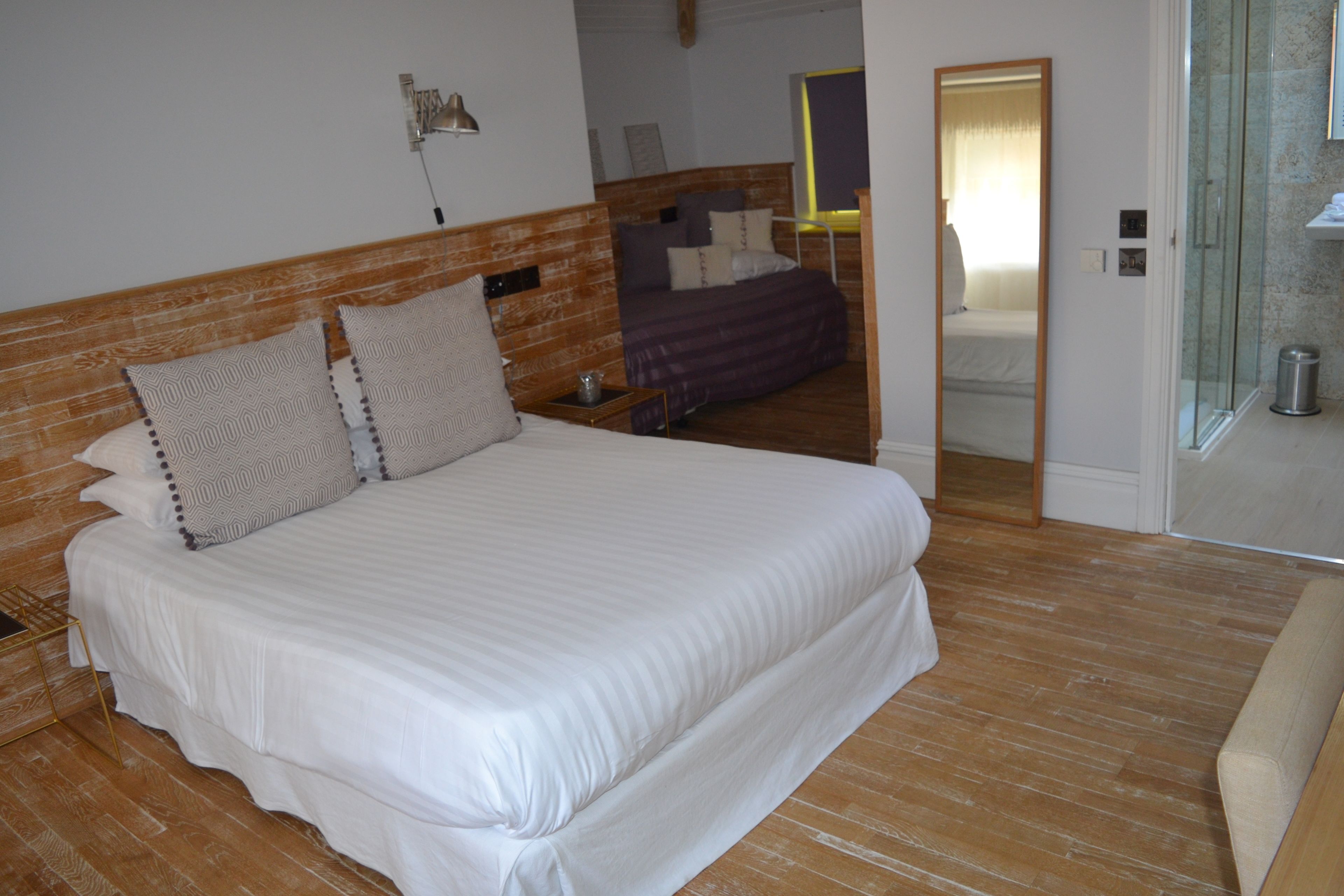A bedroom with a wooden headboard, a large bed with white bedding, a bedside table, and a mirror.