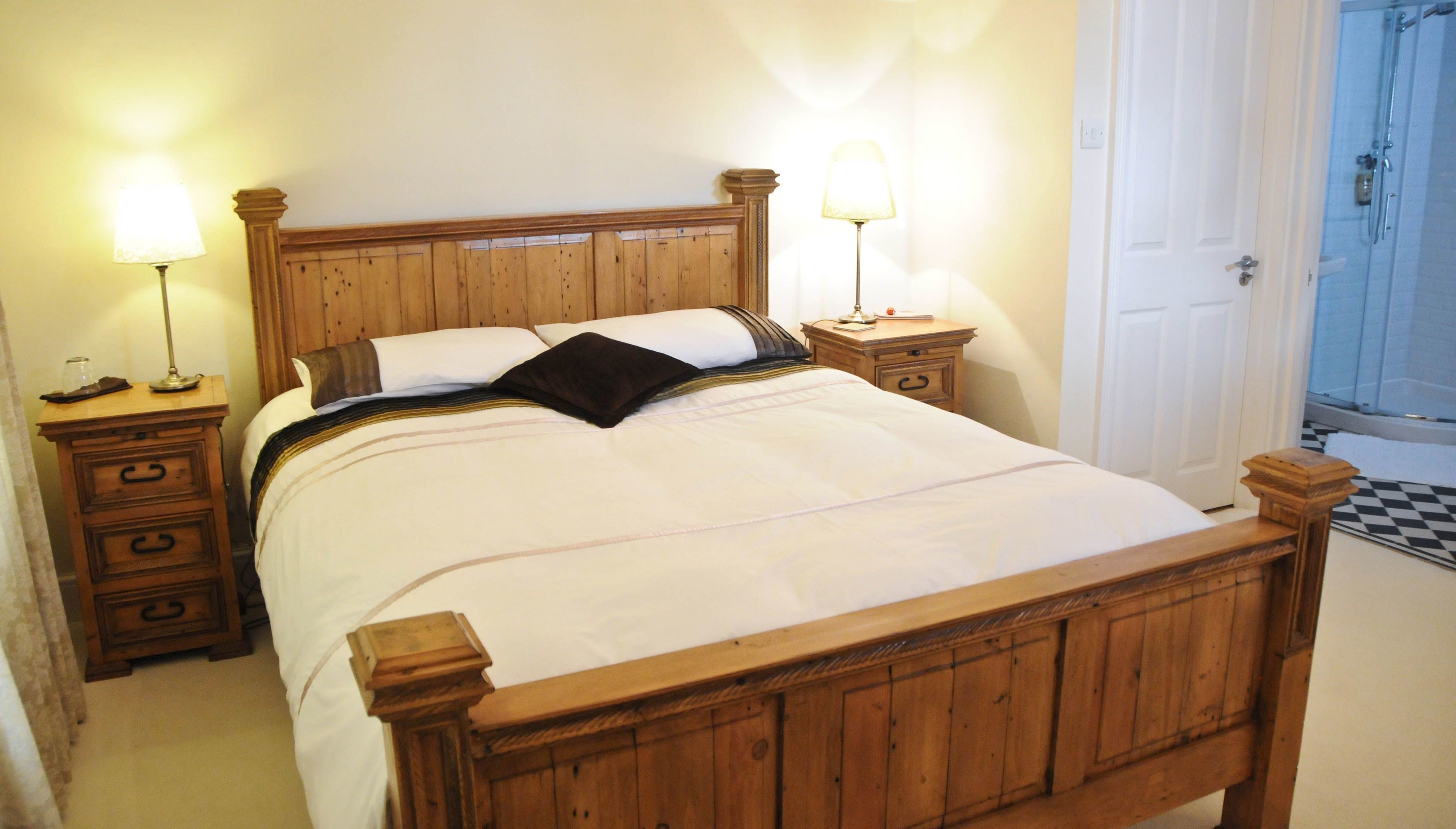 A wooden four-poster bed with a white bedspread, two bedside tables with lamps, and a wooden nightstand with drawers.