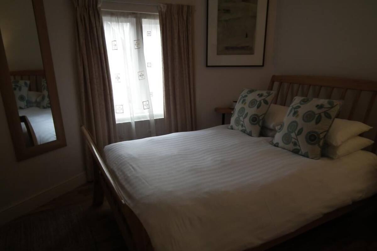 A bedroom with a large bed, a wooden headboard, a bedside table, a mirror, and a window with curtains.