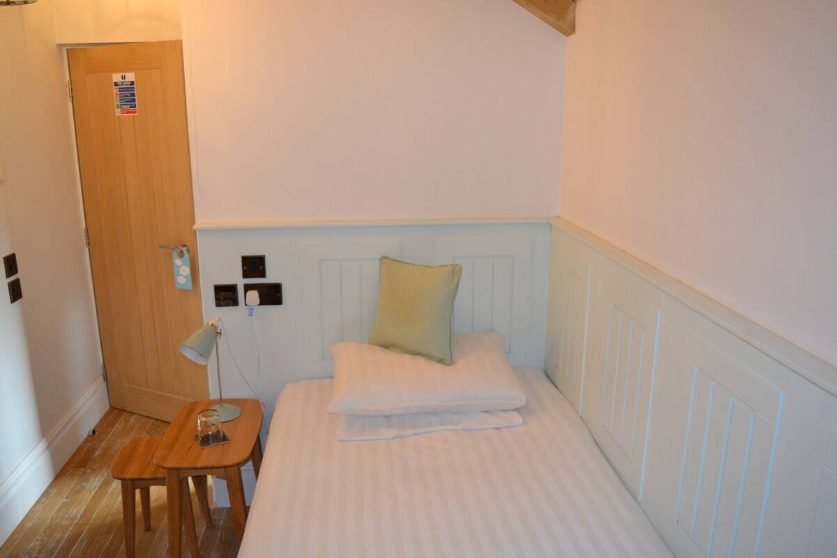 A small, neatly arranged bedroom with a single bed, a bedside table, and a lamp.