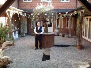 A courtyard with a central tree, surrounded by potted plants and a gravel path.