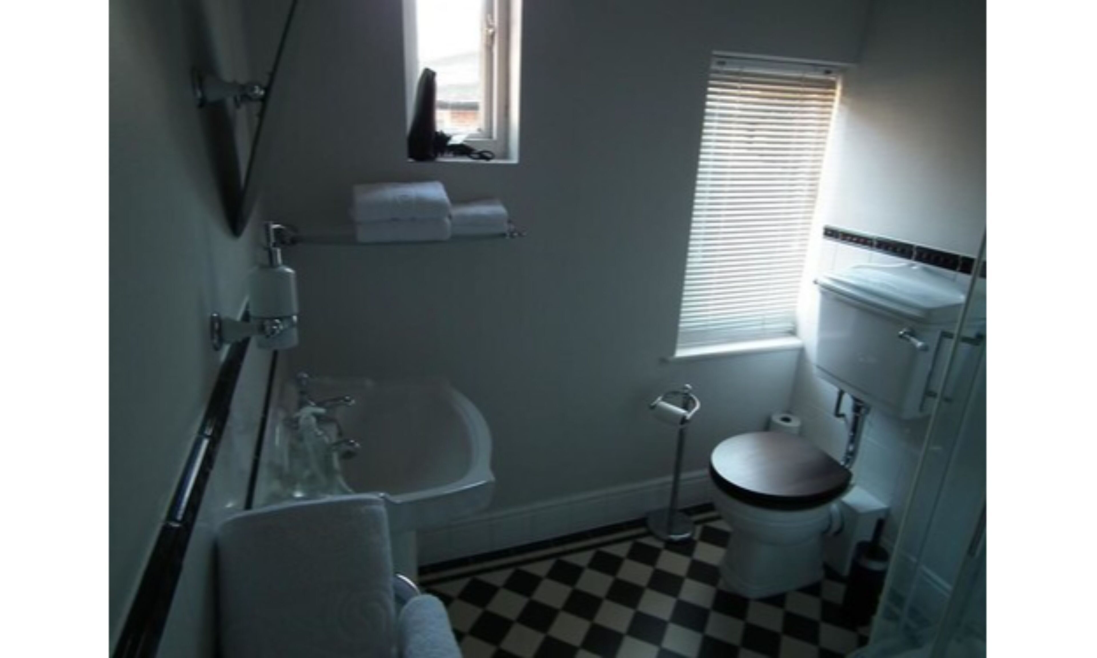 A bathroom with a bathtub, toilet, and sink. There is a window with blinds and a towel hanging on the wall.