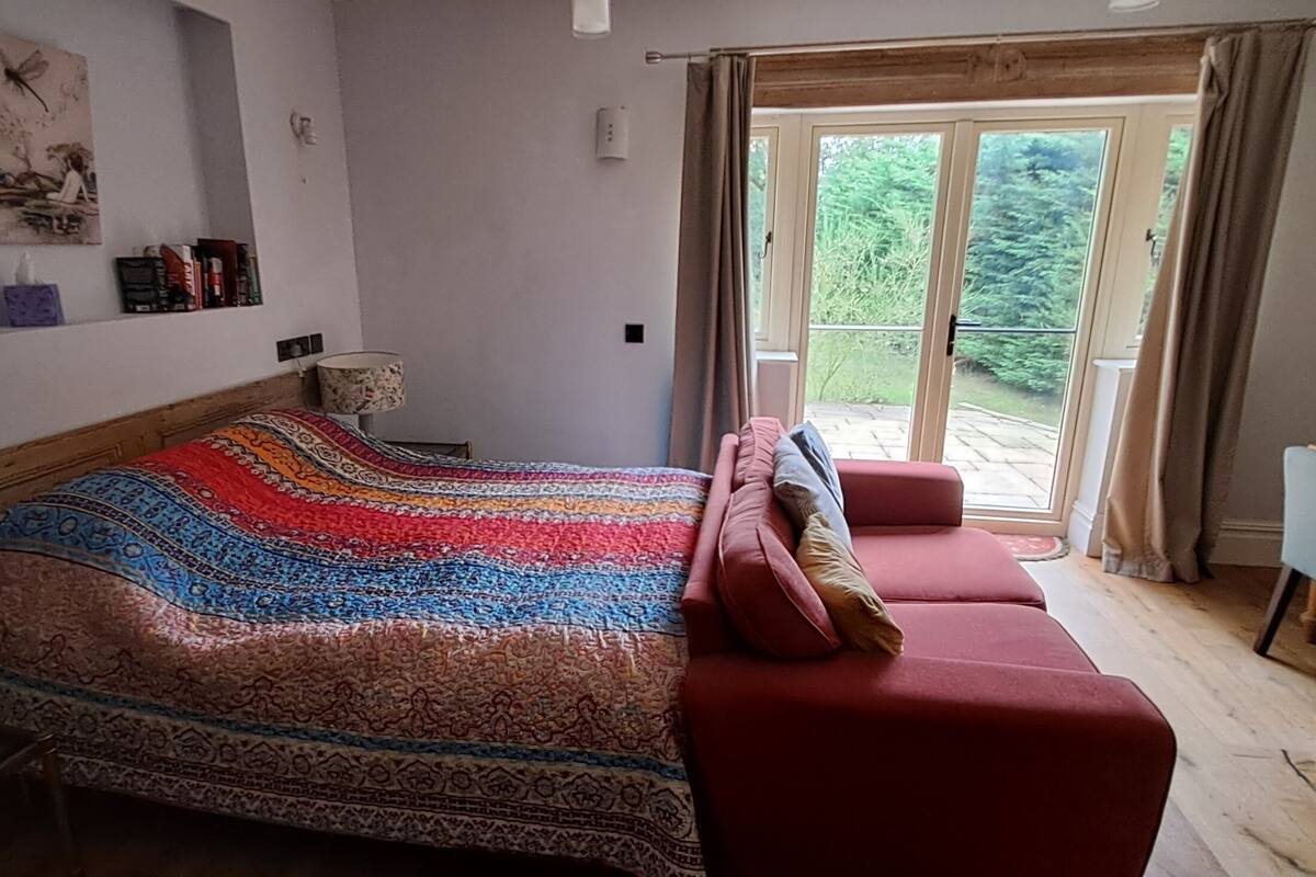 A bedroom with a bed, a desk, and a view of the outdoors.