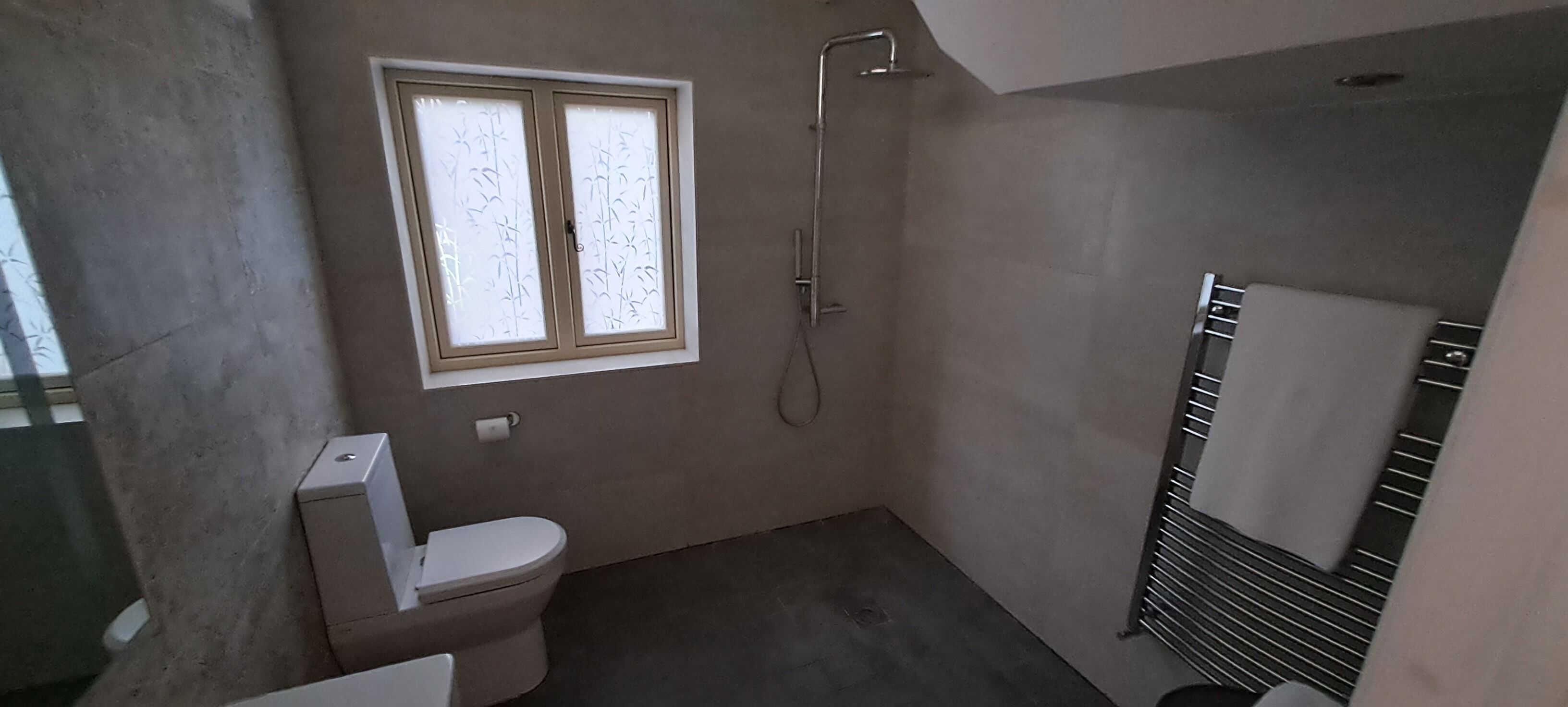 A small bathroom with a toilet, a window, and a shower.