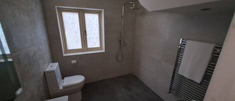 A small bathroom with a toilet, a window, and a shower.