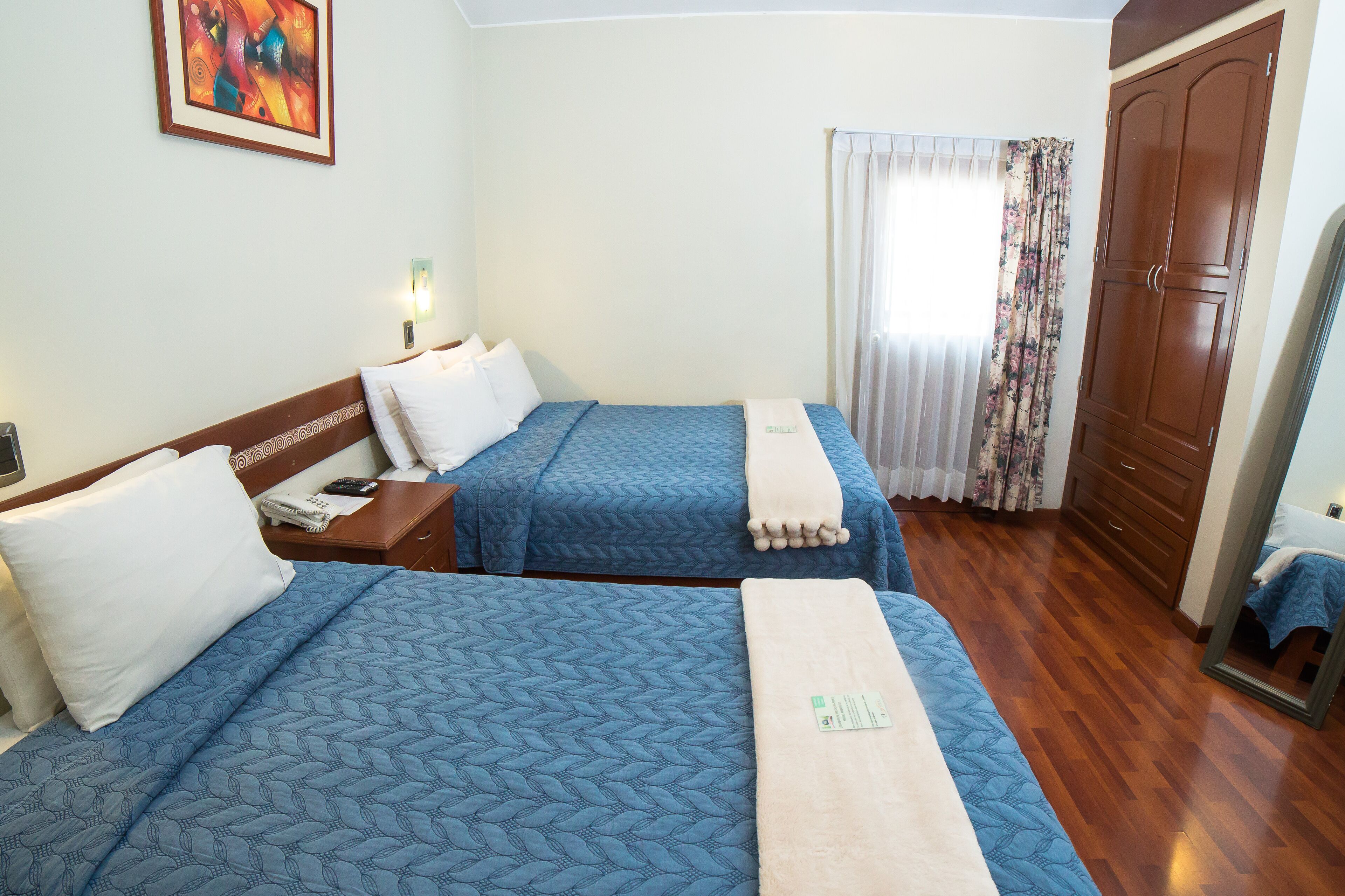 A hotel room with two beds, a wardrobe, a mirror, and a painting on the wall.