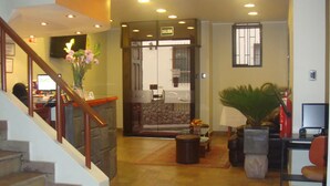 A spacious hallway with a staircase on the left, a reception desk, and a seating area with a plant on the right. - Antawasi Cusco (Cusco)