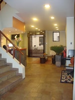 Un pasillo espacioso con una escalera a la izquierda, una recepción y una zona de estar con una planta a la derecha.