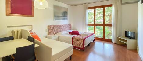 A hotel room with a bed, a desk, a chair, a TV, and a window with curtains.