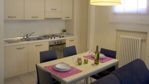 Une cuisine compacte avec un coin repas, comprenant une table dressée pour deux personnes avec une bouteille et des verres, et une suspension lumineuse au-dessus de la table.