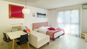 Camera d'albergo con un letto, una scrivania e una sedia. Si vede una finestra con tende, un termosifone e un condizionatore d'aria a parete.