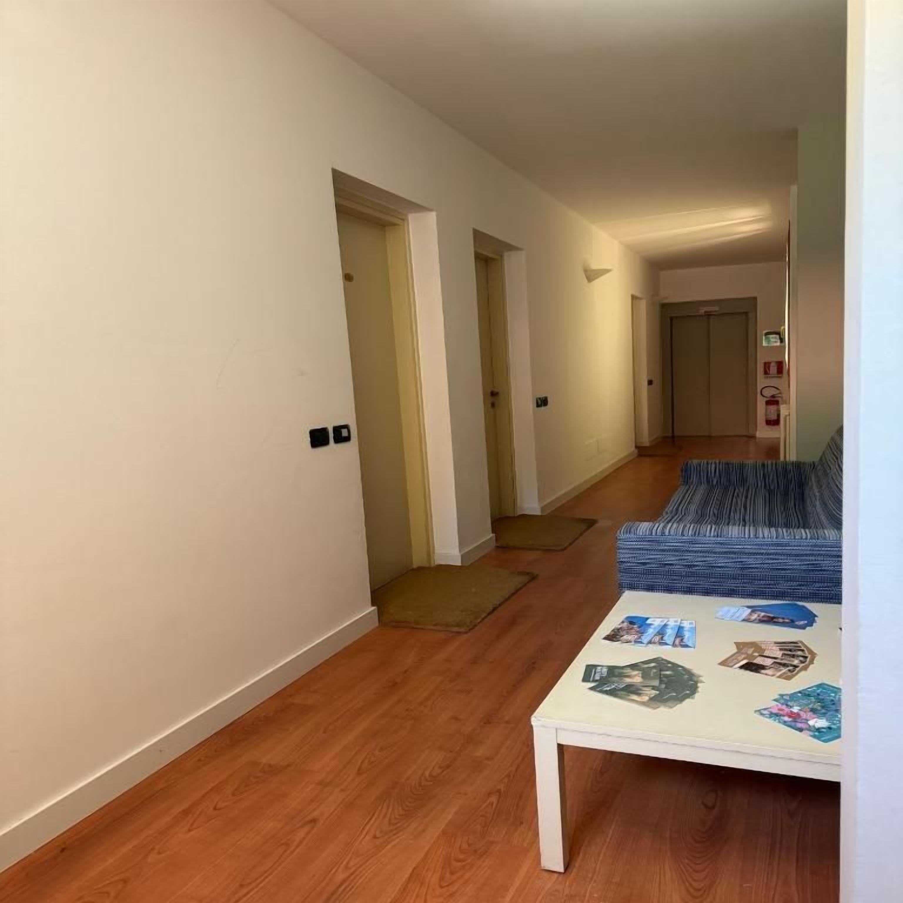 A hallway with a wooden floor, a white wall, and a blue sofa with a patterned cushion.