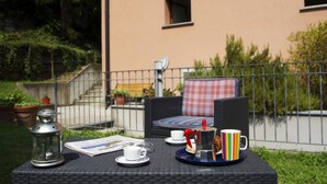 Un espace extérieur aménagé avec une table en osier, deux chaises, une lanterne, une cafetière et une tasse colorée.