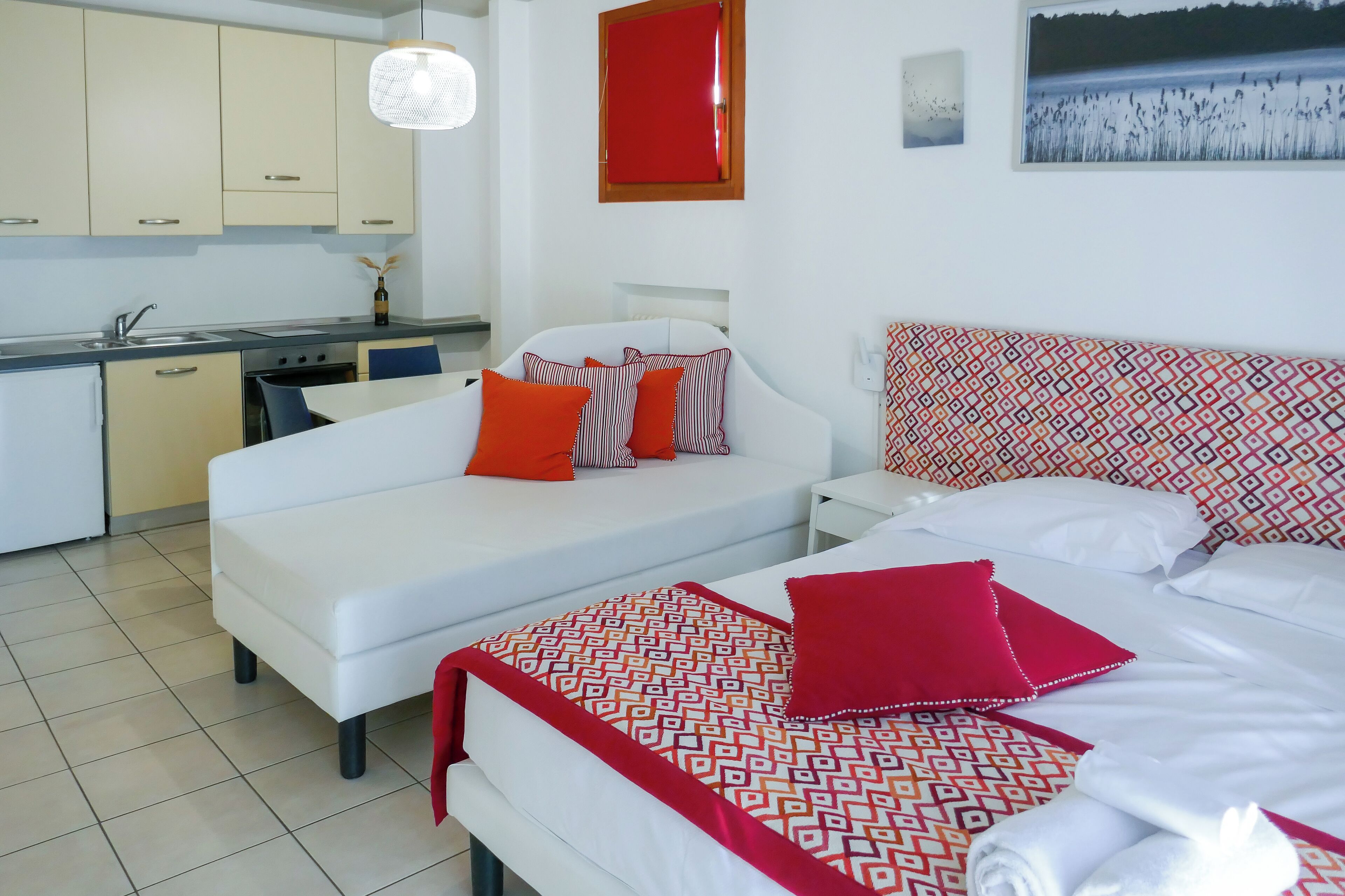 A modern hotel room with a kitchenette, a bed with patterned bedding, and a view of a natural landscape.
