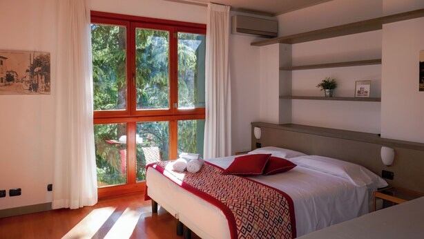 Une chambre d’hôtel avec une grande fenêtre, un lit recouvert d’une couvre-lit à motifs, une table de chevet et un climatiseur fixé au mur.