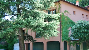 Un bâtiment à la façade rose, aux volets verts, avec un arbre au premier plan.