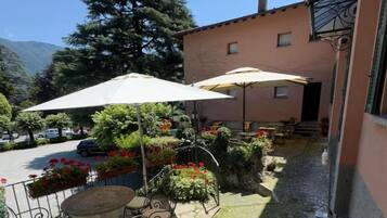Une terrasse extérieure avec une table et des chaises, entourée de plantes en pot et d’un grand parasol.