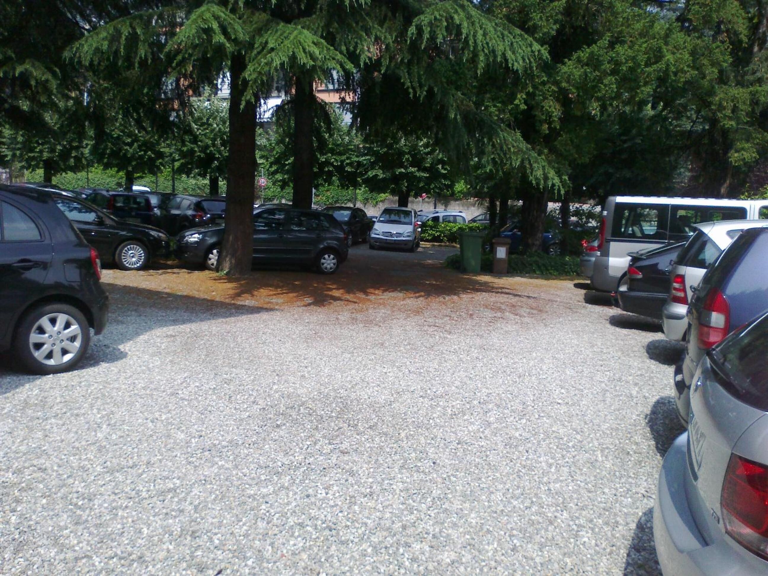 Un estacionamiento con varios coches y un autobús, rodeado de árboles.